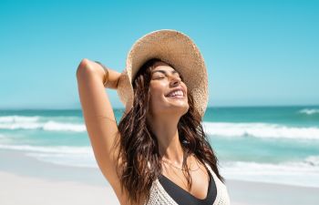 Beautiful woman wearing a straw hat enjoying a sunny day on a beach.
